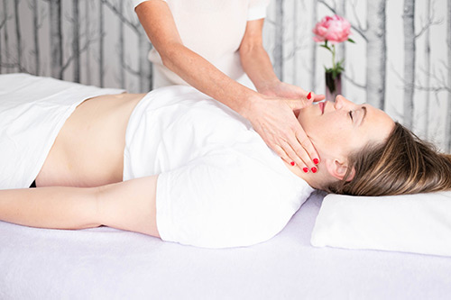 Patientin liegt auf einer Liege und Osteopathin Hilke Laue macht eine Lymphdrainage an ihrem Hals.